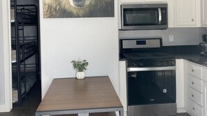 Une cuisine moderne avec des meubles blancs, un four à micro-ondes en acier inoxydable et un four traditionnel. On y trouve une table en bois, deux bancs et une plante en pot.