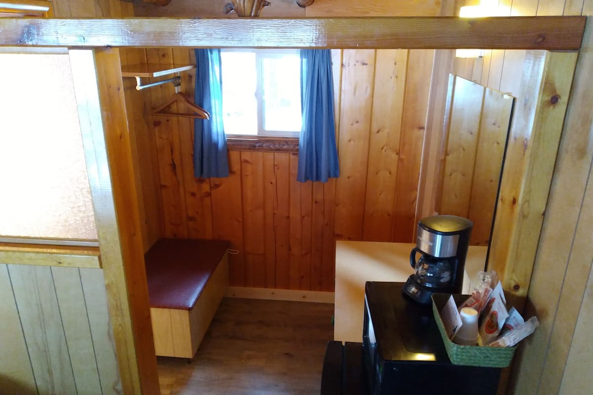Uma cabana de madeira compacta com uma pequena cozinha, um banco e uma janela com cortinas.