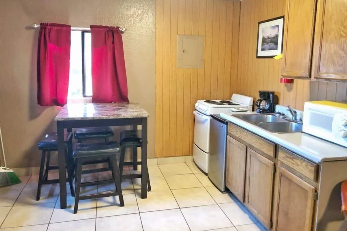 Uma cozinha compacta com mesa de jantar, cadeiras, fogão, lava-louças e armários de madeira.