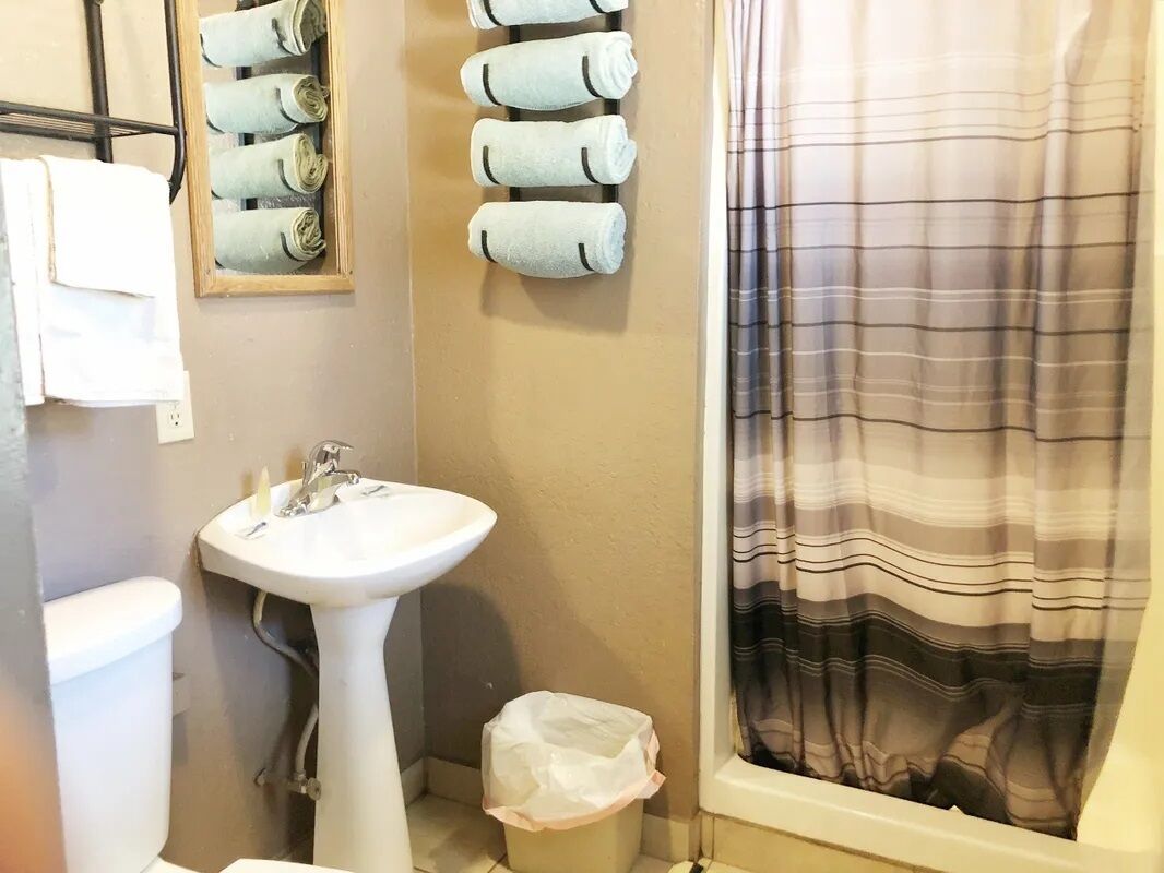 A bathroom with a white sink, a toilet, a towel rack with rolled towels, and a striped shower curtain.