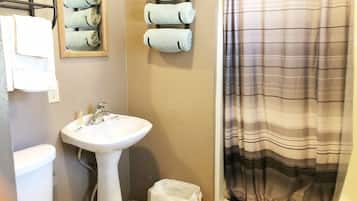A bathroom with a white sink, a toilet, a towel rack with rolled towels, and a striped shower curtain.