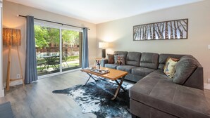 Ein modernes Wohnzimmer mit einer Couch, einem Couchtisch und einem großen Fenster mit Vorhängen.