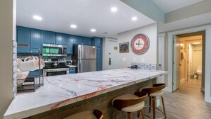 Eine moderne Küche mit blauen Schränken, einer Marmorarbeitsplatte, Edelstahlgeräten und einer Uhr an der Wand.