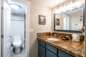 A bathroom with a white toilet, a sink with a marble countertop, and a large mirror above the sink. - Park Station by Luxury Mountain (Park City)