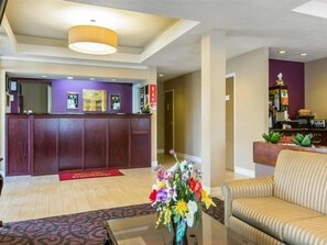 A reception area with a wooden reception desk, a vase of flowers, and a sofa. - Econo Lodge Stockbridge (Stockbridge)