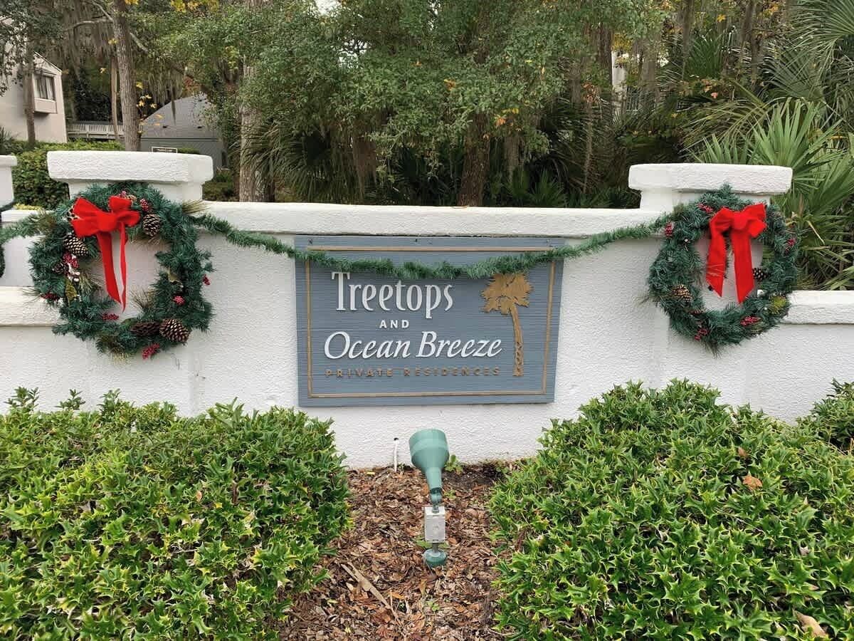 A sign for 'Treetops and Ocean Breeze' private residences with a decorative wreath and a small green planter.