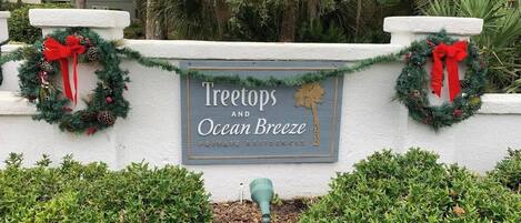 A sign for 'Treetops and Ocean Breeze' private residences with a decorative wreath and a small green planter.