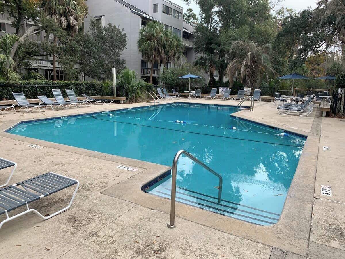 Una piscina rectangular con una escalera metálica y sillones de descanso alrededor.