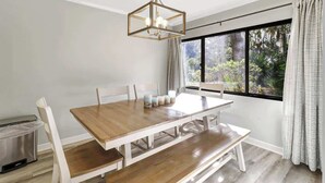 A dining area with a wooden table and benches, a hanging light fixture, and a window with a view of greenery. - Poolside Beach Villa 2 bed 2 & one half bath-Pet Friendly (Hilton Head Island)