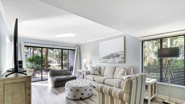 A modern living room with a sofa, ottoman, and a television on a wooden stand. - Poolside Beach Villa 2 bed 2 & one half bath-Pet Friendly (Hilton Head Island)
