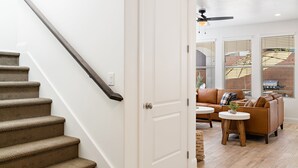 A staircase with carpeted steps and a handrail, leading to a room with a brown leather sofa, a small round table, and a ceiling fan. - LeBlanc 5 Bedroom!  5 Bath! Firepit! Dog Friendly! (Washington)
