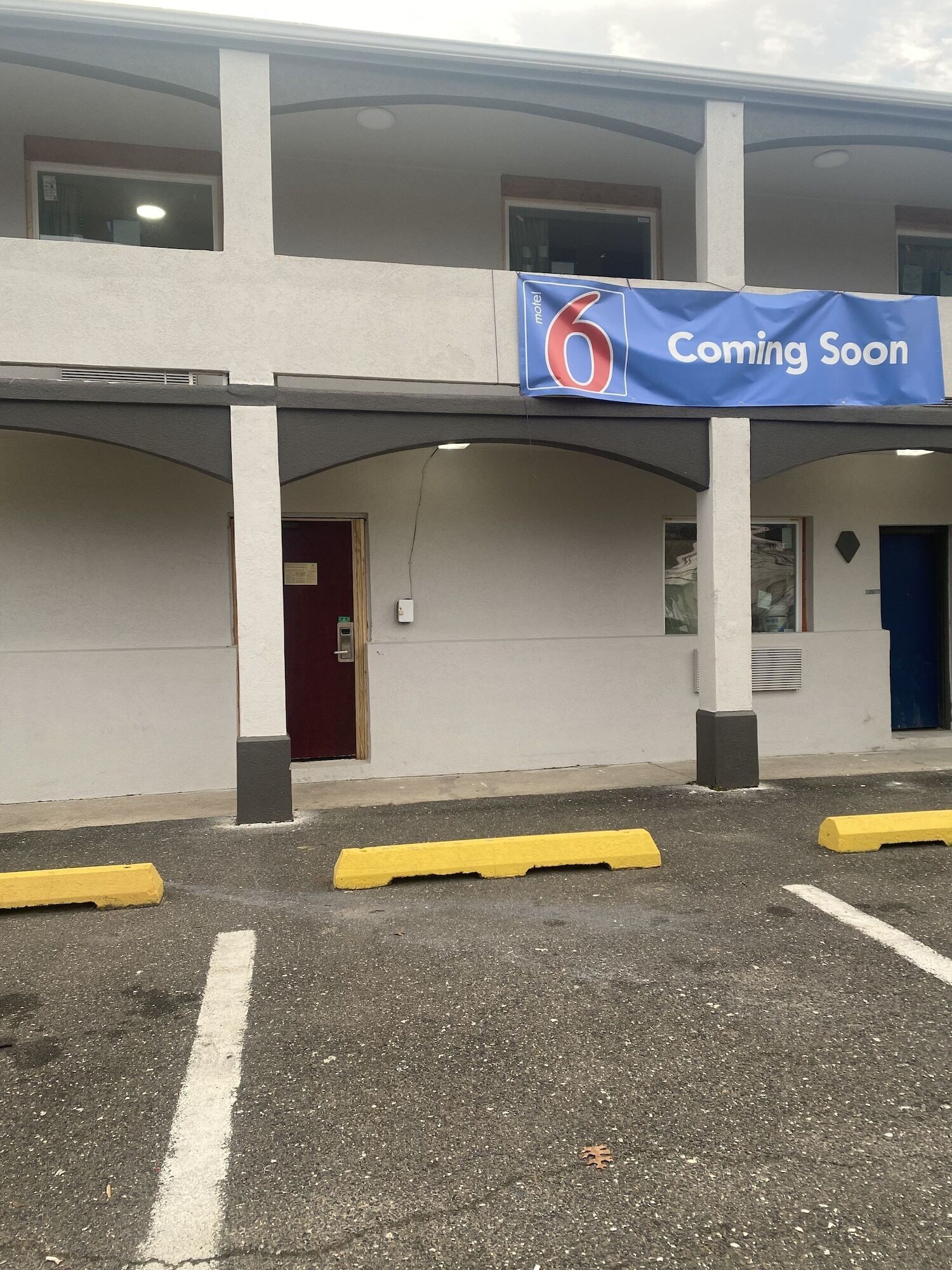 Een gebouw met een 'Binnenkort geopend' bord, een rode deur en gele parkeerpalen.