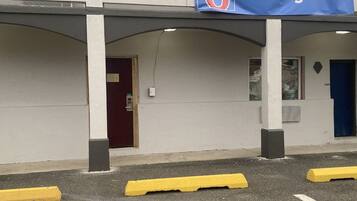 Een gebouw met een 'Binnenkort geopend' bord, een rode deur en gele parkeerpalen.