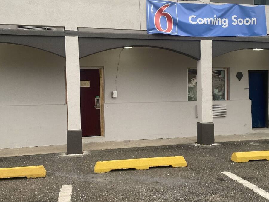 Een gebouw met een 'Binnenkort geopend' bord, een rode deur en gele parkeerpalen.