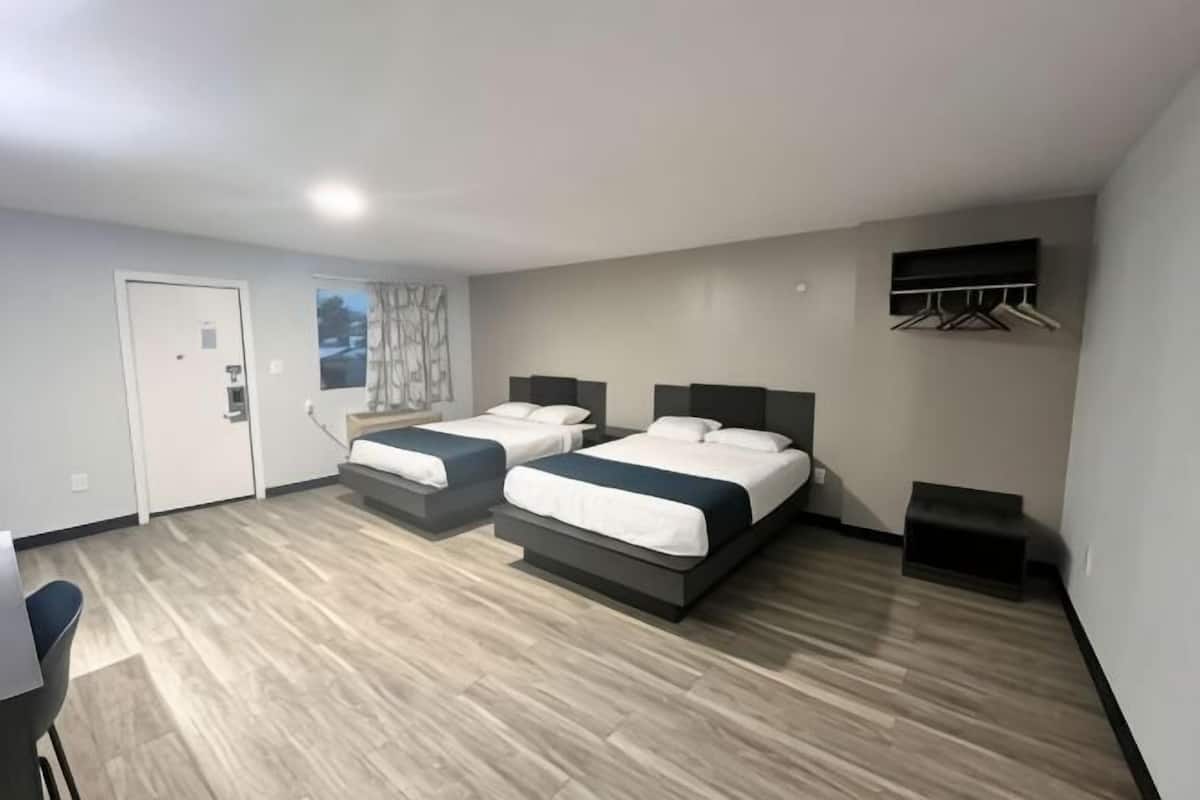 A hotel room with two beds, a desk, and a window.