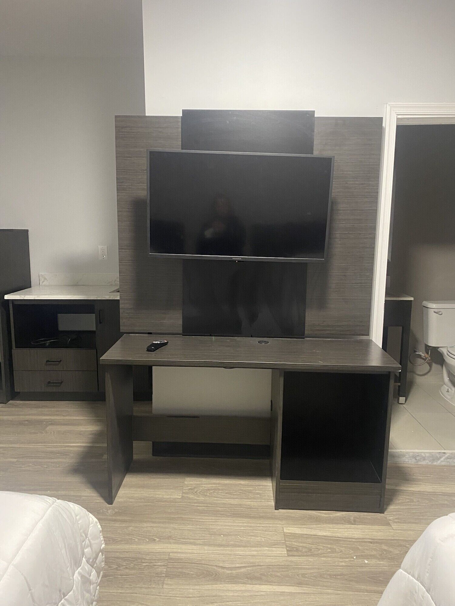 Et moderne værelse med et indbygget tv på en træpanel, et lille skrivebord med stol og et toilet i hjørnet.
