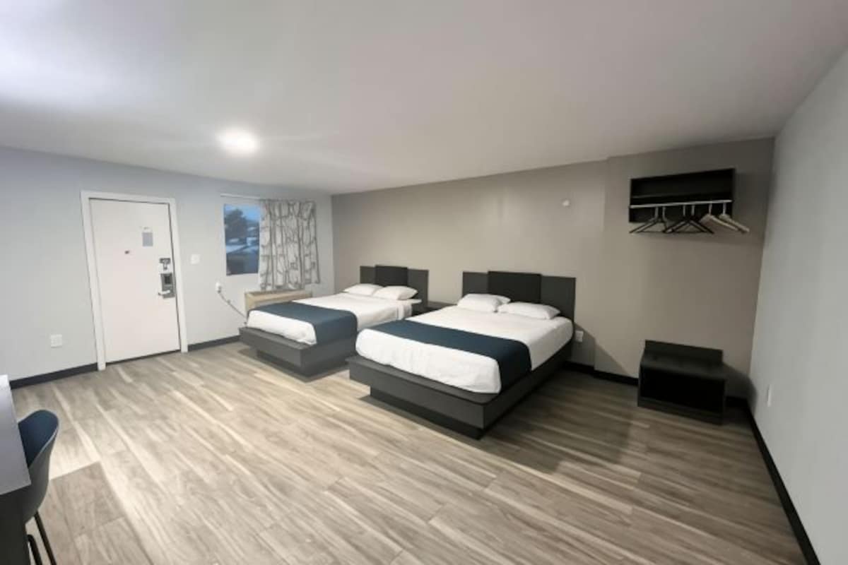 A hotel room with two beds, a desk, and a window.