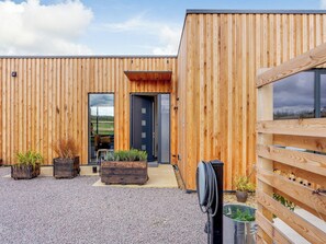 A modern wooden building with a gravel driveway, a door, and potted plants.