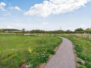 A gravel path curving through a grassy field with a small pond and a fence in the distance. - Buttercup Lodge - UK36655 (Boothby Pagnell)