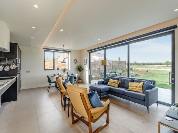 A modern living room with a large window, a dining area, and a kitchen.