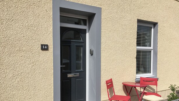 Een gebouw met een zwarte deur, een raam met luiken, en een bord met het cijfer 14.