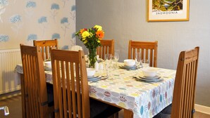 Een eetkamer met een tafel voor zes personen, omringd door houten stoelen, een bloevas en een lijst met een foto aan de muur.