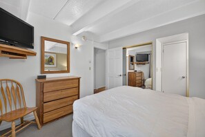 Une chambre d’hôtel avec un lit, une commode en bois, une chaise, un téléviseur et un miroir.
