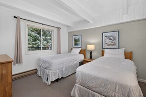 Una camera d'albergo con due letti singoli, una finestra con tende, un comodino con una lampada e quadri appesi al muro.
