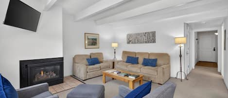 A living room with a fireplace, two sofas, a coffee table, and a television mounted on the wall.