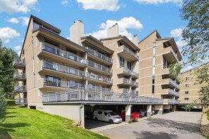 Un edificio residenziale a più piani con balconi, un'area parcheggio coperta e un prato.