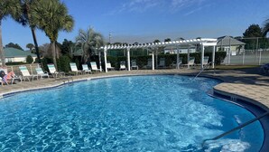 Una piscina cristalina con sillones de descanso y una pérgola.