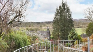 Un paysage rural avec une maison en pierre, une clôture en métal et une variété d’arbres et d’arbustes.