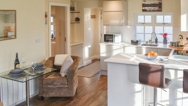 Une cuisine moderne dotée d’un îlot central, d’un coin repas avec une table en verre et d’un espace salon confortable avec un fauteuil marron.