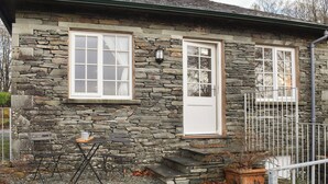 Une maison en pierre avec deux fenêtres, une porte et un petit espace extérieur aménagé avec une table et des chaises.