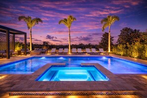 A swimming pool with lounge chairs and palm trees, surrounded by a landscaped garden. - Electronic Ice Castle | 8 Bedroom Villa w/ Themed Bedrooms, Game Room, Theater Room, & Private Pool (Kissimmee)