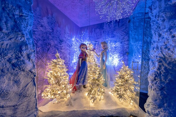 Decoración invernal con dos figuras, un paisaje nevado y árboles de Navidad iluminados.