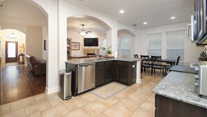 A modern kitchen with dark cabinetry, a stainless steel dishwasher, and a granite countertop. - Limestone Ranch House-4 Bedroom 3 Bath House (Cibolo)