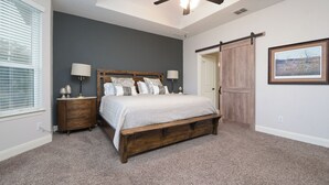 A bedroom with a large bed, a ceiling fan, a wooden bench, a nightstand, and a door with a barn-style door. - Limestone Ranch House-4 Bedroom 3 Bath House (Cibolo)