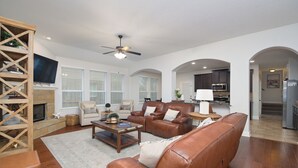 A spacious living room with a fireplace, leather sofas, a coffee table, and a TV mounted on the wall. - Limestone Ranch House-4 Bedroom 3 Bath House (Cibolo)