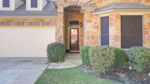 A two-story house with a stone facade, a garage, and a front door with a decorative glass panel. - Limestone Ranch House-4 Bedroom 3 Bath House (Cibolo)