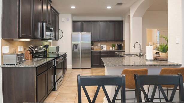 A modern kitchen with dark cabinetry, stainless steel appliances, and a central island with seating. - Limestone Ranch House-4 Bedroom 3 Bath House (Cibolo)