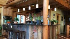 Cocina rústica con vigas de madera, una barra con taburetes y plantas en macetas.