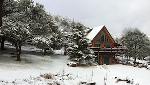 Una cabaña de madera con balcón, rodeada de árboles y rocas cubiertas de nieve.