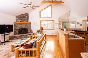 A cozy living room with a stone fireplace, wooden furniture, and a kitchen area with a stove and sink. - The Smitty Place- family friendly, near downtown, great parking! (McCall)