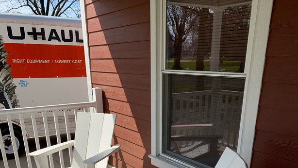 Un furgone U-Haul parcheggiato di fronte a una casa con un portico e sedie Adirondack bianche.