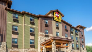 Un hotel de varios pisos con fachada verde y marrón, un letrero que dice "My Place Hotels" y una base de piedra.