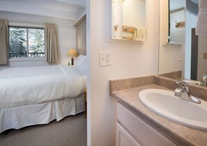 A hotel room with a bed, a bathroom with a sink and mirror, and a window with curtains. - Vail 2-bedroom condo with pool/hottub (Vail)