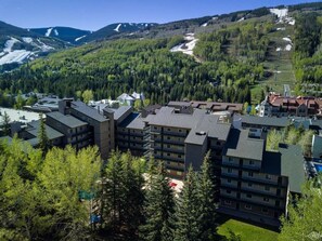 A multi-story hotel with a modern architectural design, surrounded by lush greenery and mountains in the background. - Vail 2-bedroom condo with pool/hottub (Vail)