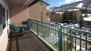 A balcony with a table and chairs, overlooking a snowy landscape with buildings and mountains. - Vail 2-bedroom condo with pool/hottub (Vail)