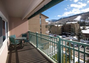 A balcony with a table and chairs, overlooking a snowy landscape with buildings and mountains. - Vail 2-bedroom condo with pool/hottub (Vail)